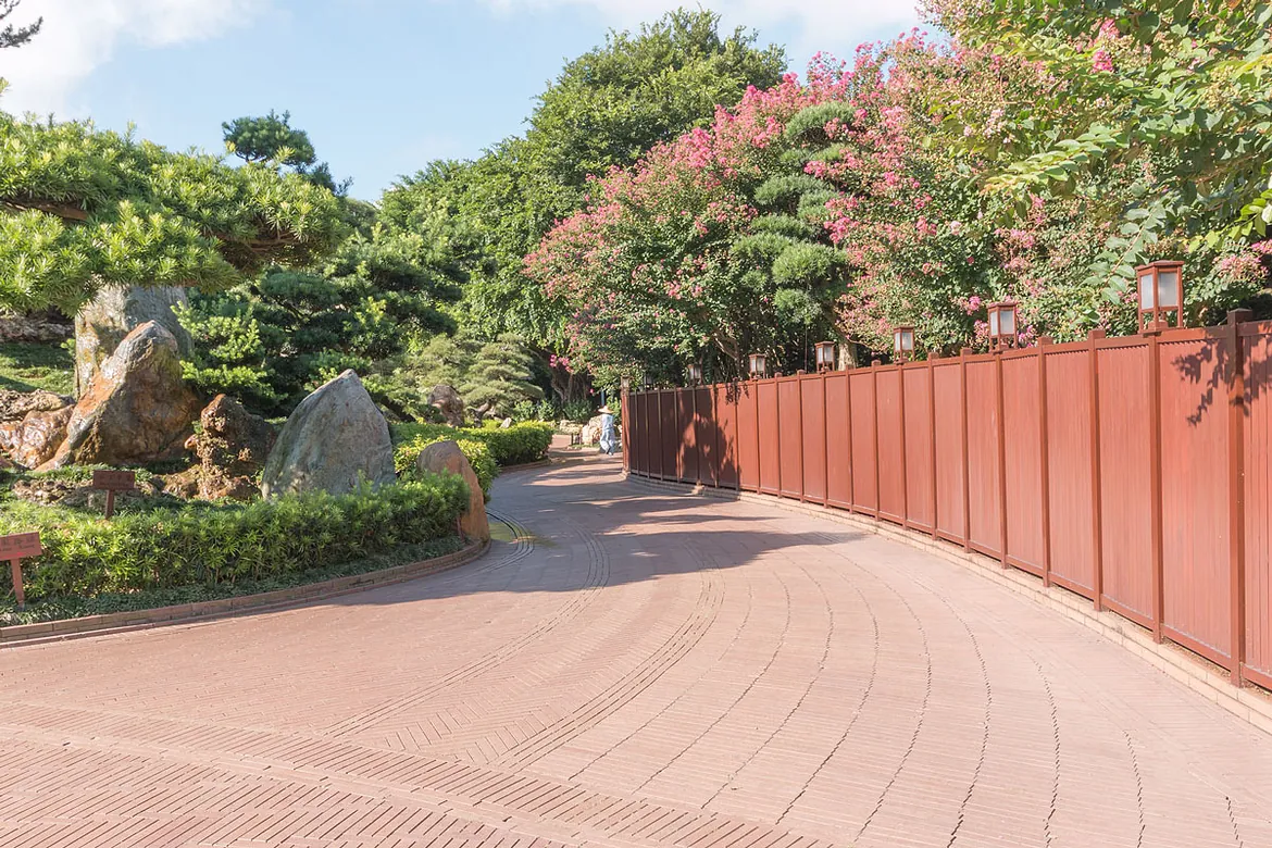 Long red-toned paved driveway beside garden planting and fencing